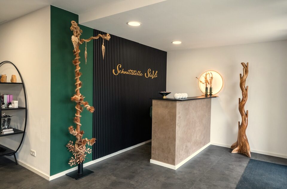 Empfang des Salons mit dunkler Lamellenwand, goldenem Schriftzug und grüner Wand