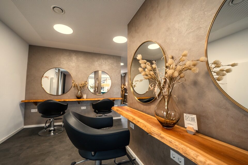 Frisierplätze mit schwarzen Stühlen, runden Spiegeln und einer Ablage aus Holz im Salon